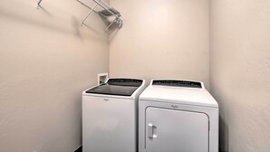 Pesuhuoneessa on kaksi valkoista Whirlpool-merkkiä olevaa pesukonetta ja seinällä metallinen pyykiteline.