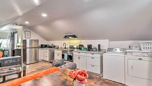 A modern kitchen with white cabinets, stainless steel appliances, and a dining area with a wooden table and orange cushion. - Fayetteville Apartment w/ Yard: Pets Welcome! (Fayetteville)