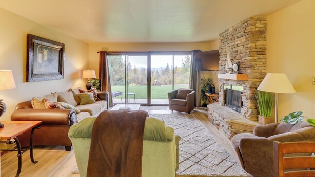 A spacious living room with a fireplace, comfortable seating, and a large sliding glass door leading to a patio. - Bigfork Condo w/ Hot Tub Access, By Lake! (Bigfork)