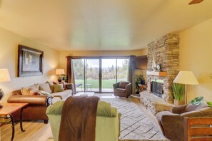 A spacious living room with a fireplace, comfortable seating, and a large sliding glass door leading to a patio. - Bigfork Condo w/ Hot Tub Access, By Lake! (Bigfork)
