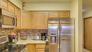 A kitchen with wooden cabinets, a stainless steel refrigerator, a microwave, a toaster, and a coffee maker. - Bigfork Condo w/ Hot Tub Access, By Lake! (Bigfork)