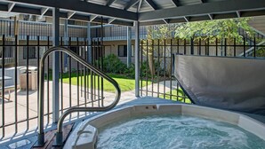 A hot tub with a metal railing and a view of a residential building in the background. - Bigfork Condo w/ Hot Tub Access, By Lake! (Bigfork)