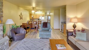 A spacious living room with a sofa, armchair, and coffee table. A dining area with chairs and a table is visible in the background. - Bigfork Condo w/ Hot Tub Access, By Lake! (Bigfork)