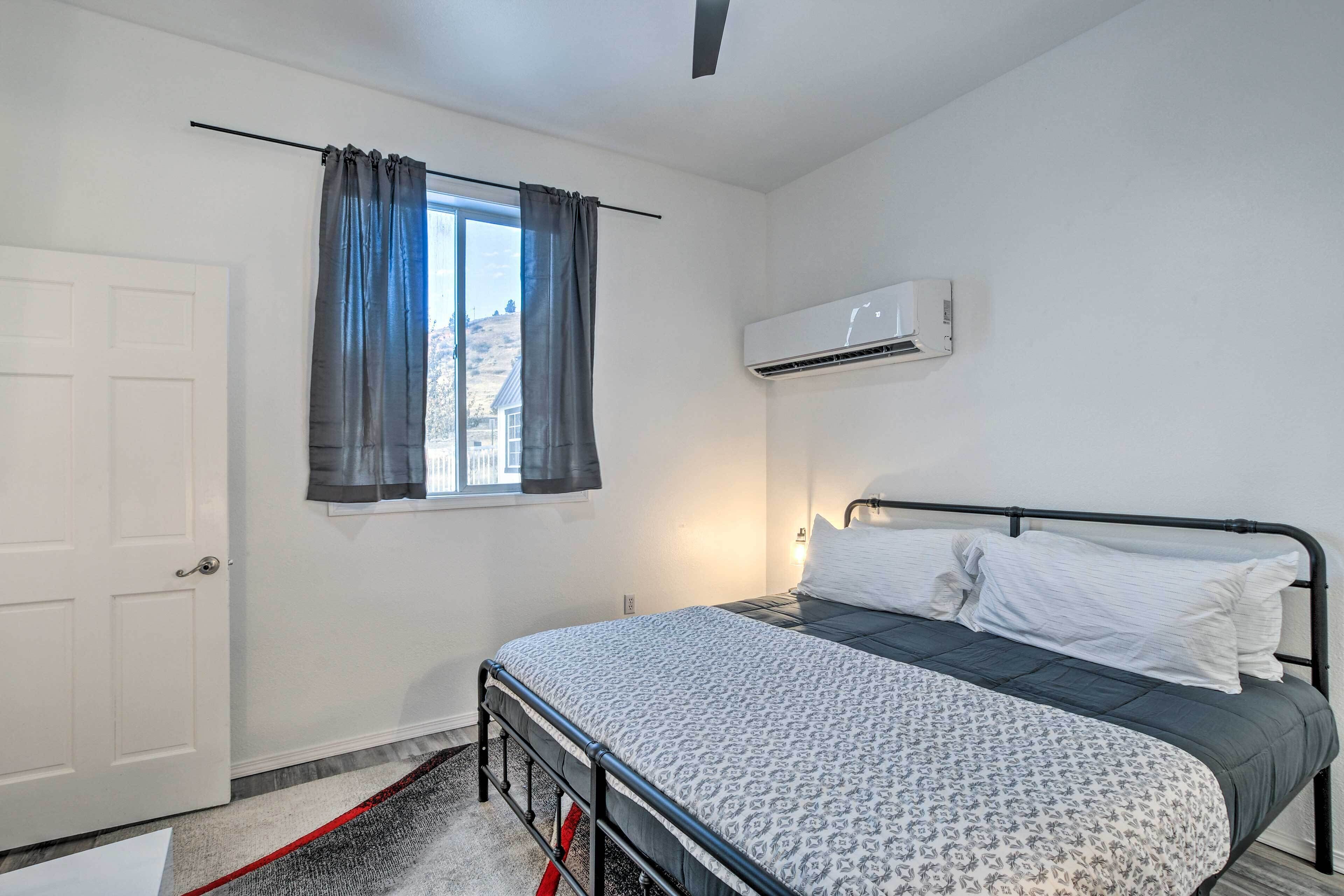 A bedroom with a bed, a window with curtains, an air conditioning unit, and a door.