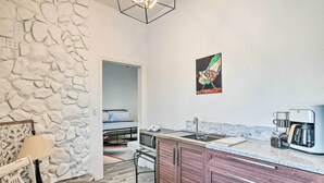 Une cuisine compacte avec un mur d’accent en pierre, un lit dans la pièce adjacente et une machine à café posée sur le plan de travail.