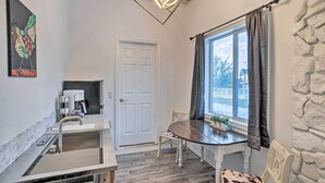 Une petite pièce comprenant un évier, une table à manger, une chaise, une fenêtre avec des rideaux et une porte.