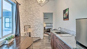 Une cuisine moderne avec un mur d’accent en pierre, un coin repas avec une table en bois et une vue dégagée sur l’extérieur grâce à une grande fenêtre.