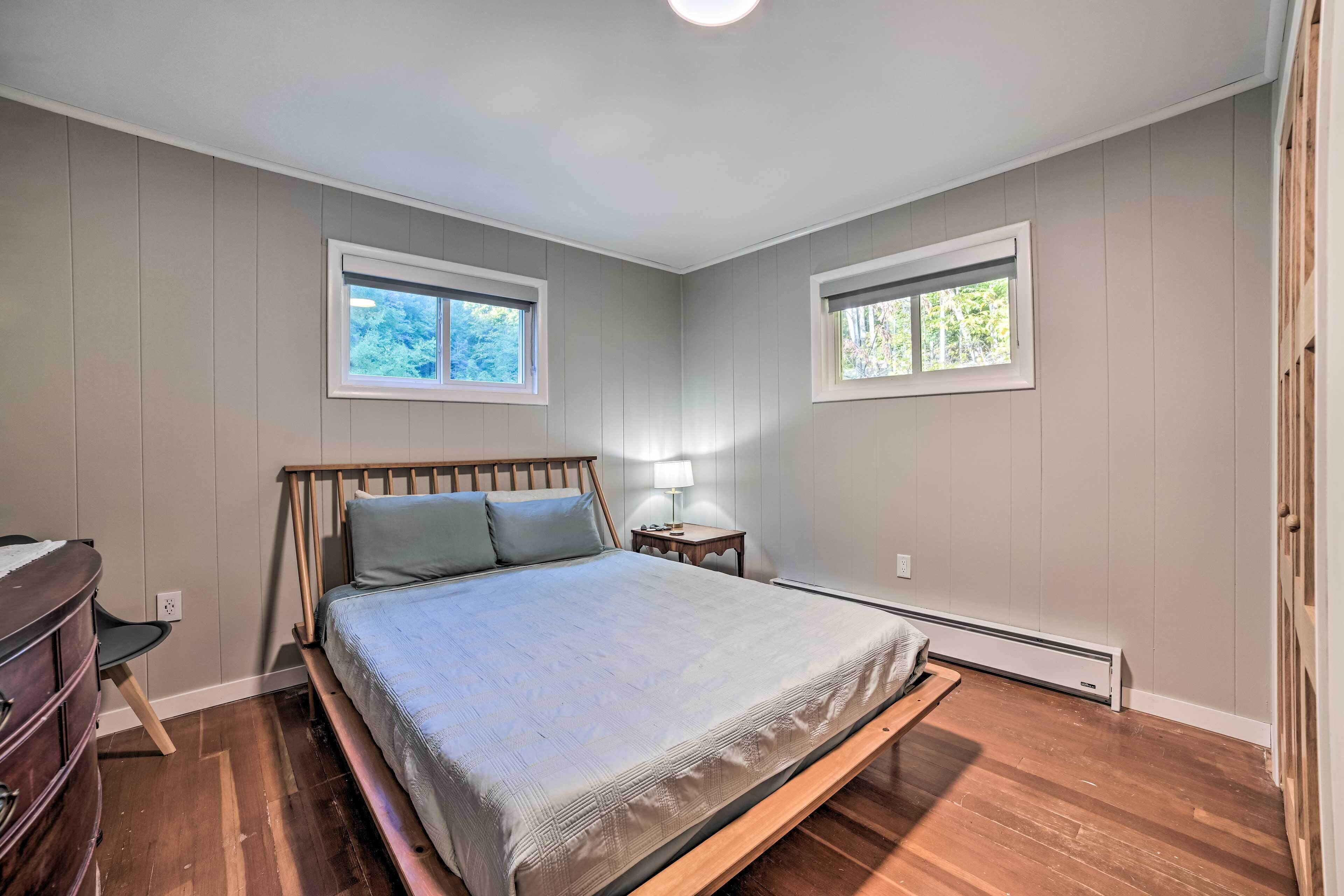 A bedroom with a bed, two windows, a nightstand, and a dresser.
