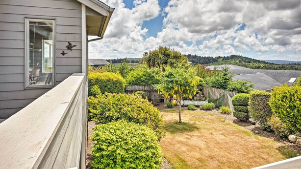 A residential property with a well-maintained garden, a wooden fence, and a clear view of the surrounding landscape. - Chic Coos Bay Home w/ Pacific Ocean Views! (Coos Bay)