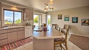 A modern kitchen with a large island, pendant lights, and a view of the outdoors. - Chic Coos Bay Home w/ Pacific Ocean Views! (Coos Bay)