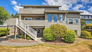 A modern two-story house with a covered staircase, a small front yard with a tree, and a clear blue sky. - Chic Coos Bay Home w/ Pacific Ocean Views! (Coos Bay)