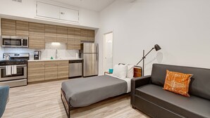 A compact living space with a kitchenette, a bed, a sofa, and a floor lamp. - Cabin 105 by 747 Lofts (Chicago)