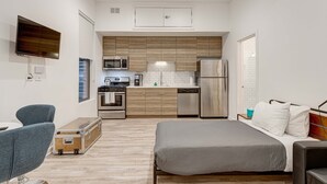 A compact hotel room with a bed, a small kitchenette, a TV, and a suitcase. - Cabin 105 by 747 Lofts (Chicago)