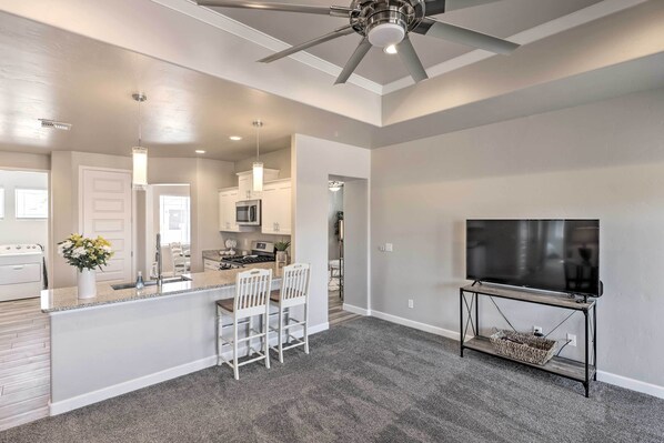 A modern living room with a TV on a stand, a ceiling fan, and a kitchen in the background.