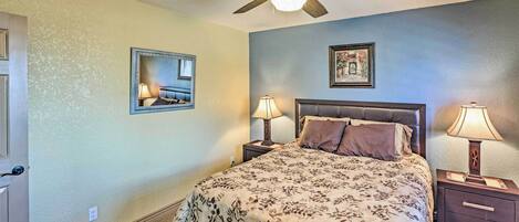 A bedroom with a bed, two bedside tables with lamps, a ceiling fan, a door, and a wall-mounted mirror.