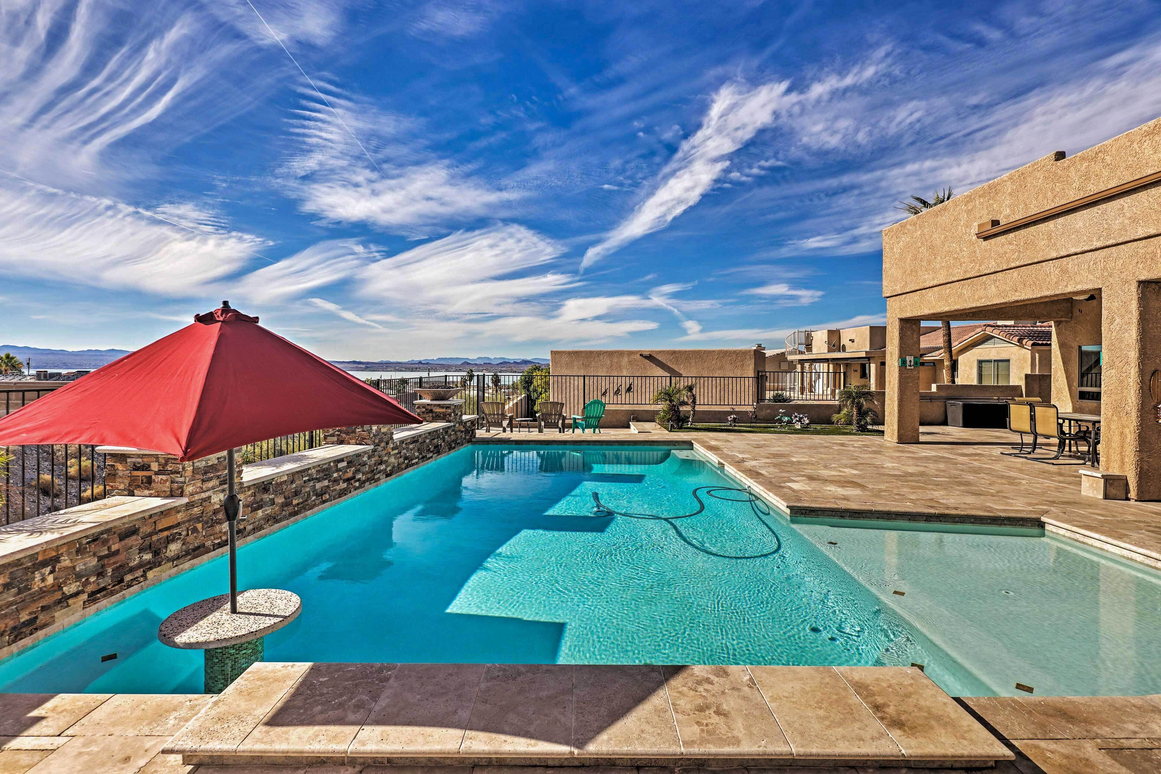 Une piscine avec un parasol rouge, des murs en pierre et un ciel bleu clair.