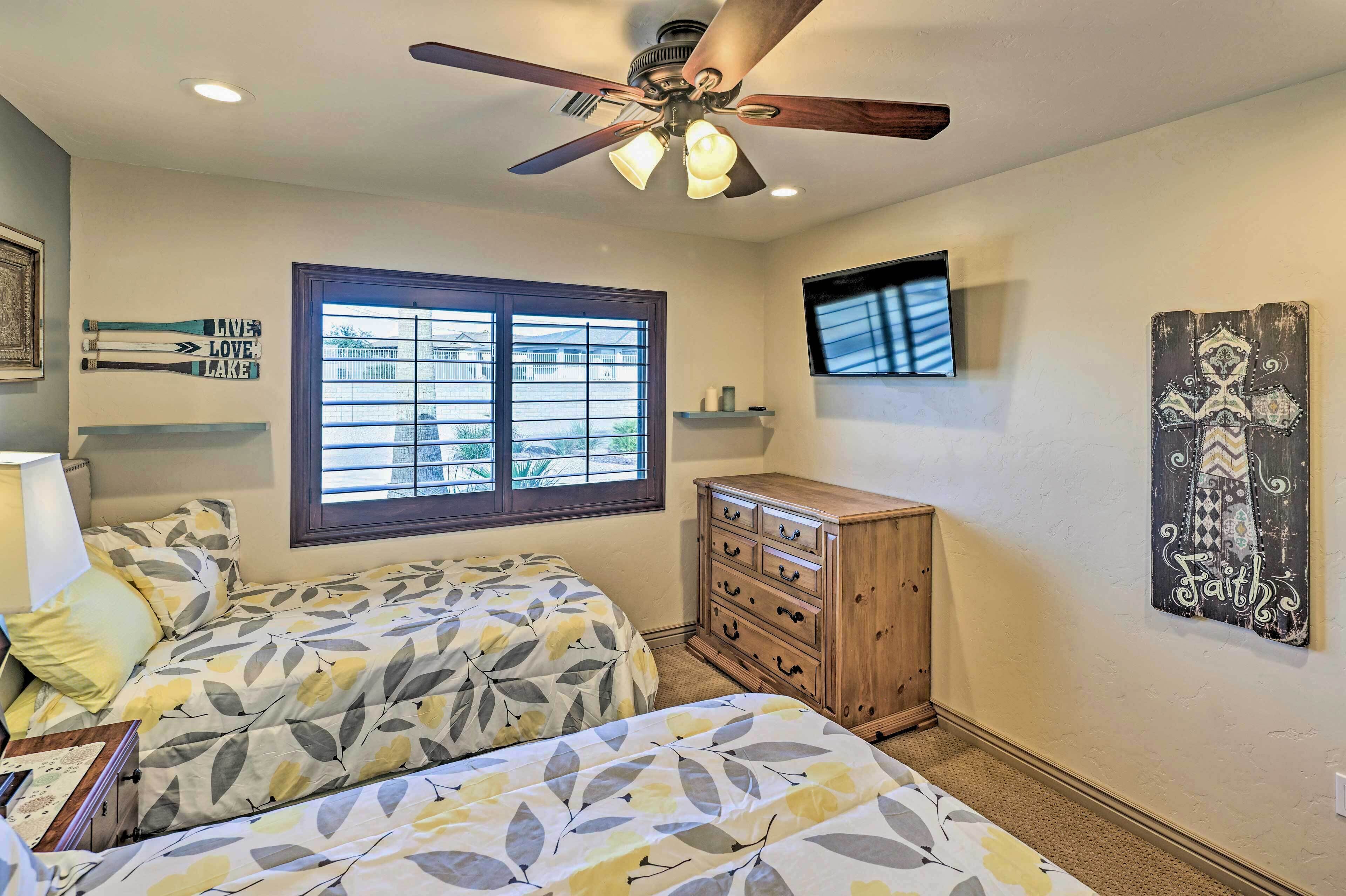 A bedroom with two beds, a ceiling fan, a window, a dresser, and a TV on the wall.