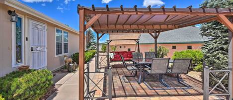 A covered patio with outdoor furniture, a pergola, and a house in the background.