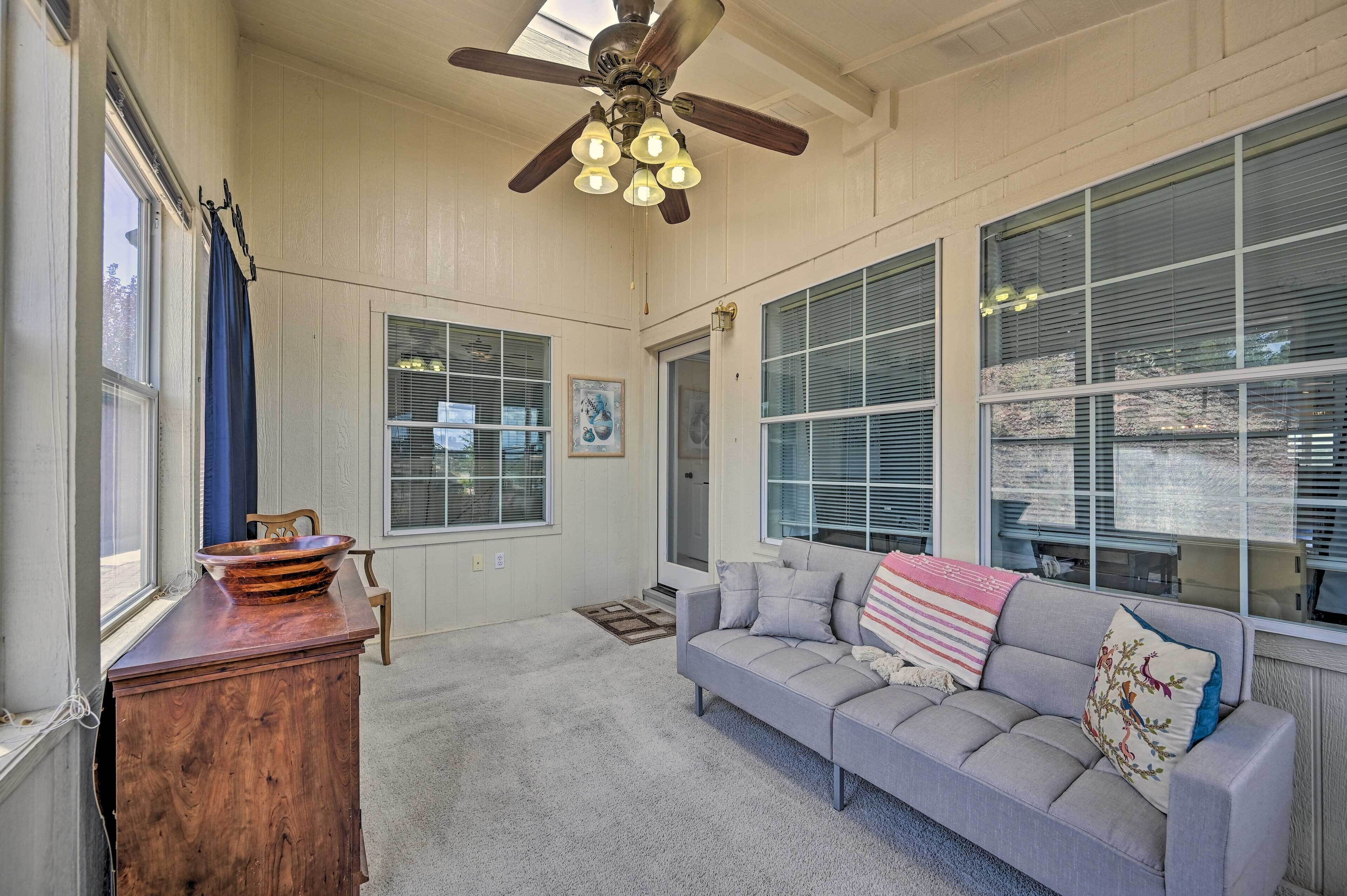 A spacious living room with a ceiling fan, large windows, a gray sofa, and a wooden cabinet.