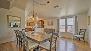 A spacious dining area with a large wooden table and chairs, a kitchen in the background, and a view through a large window. - Arizona Room, Gas Grill: Charming Payson Home! (Payson)