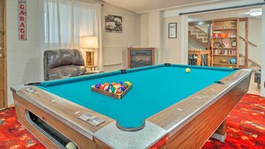A pool table with balls, a leather chair, a lamp, and a bookshelf.