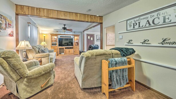 A living room with two green recliners, a wooden bench with a towel, a TV, and a 'Welcome to Our Place' sign on the wall.