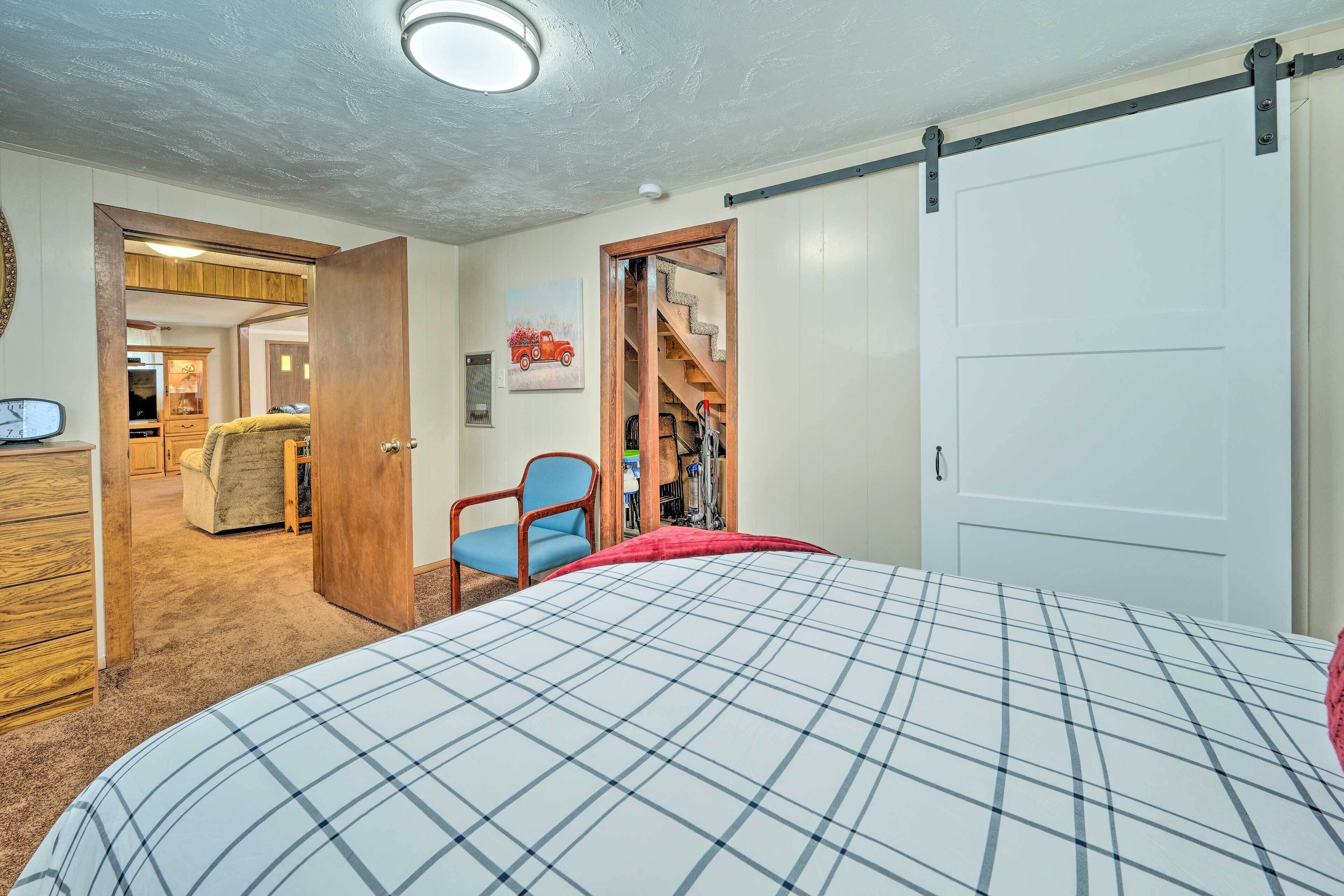 Een slaapkamer met een bed, een stoel, een kledingkast en een deur die naar een trap leidt.
