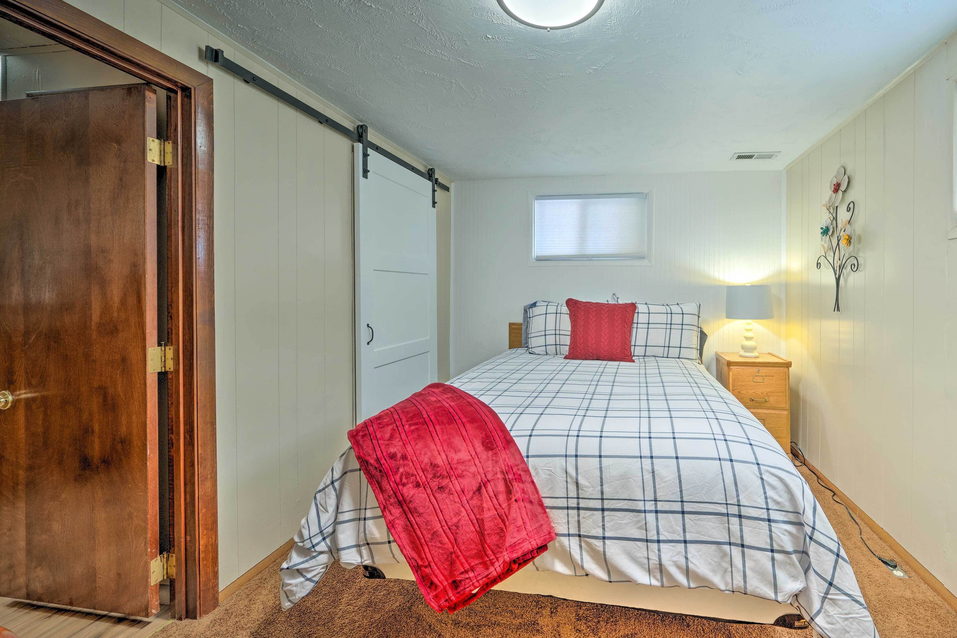 Um quarto com cama, mesa de cabeceira, luminária, janela e porta.