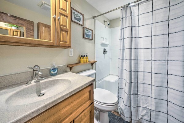 A bathroom with a granite sink, wooden cabinets, a toilet, and a shower curtain.