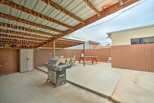 An outdoor patio with a grill, seating, and a covered area with a wooden ceiling.