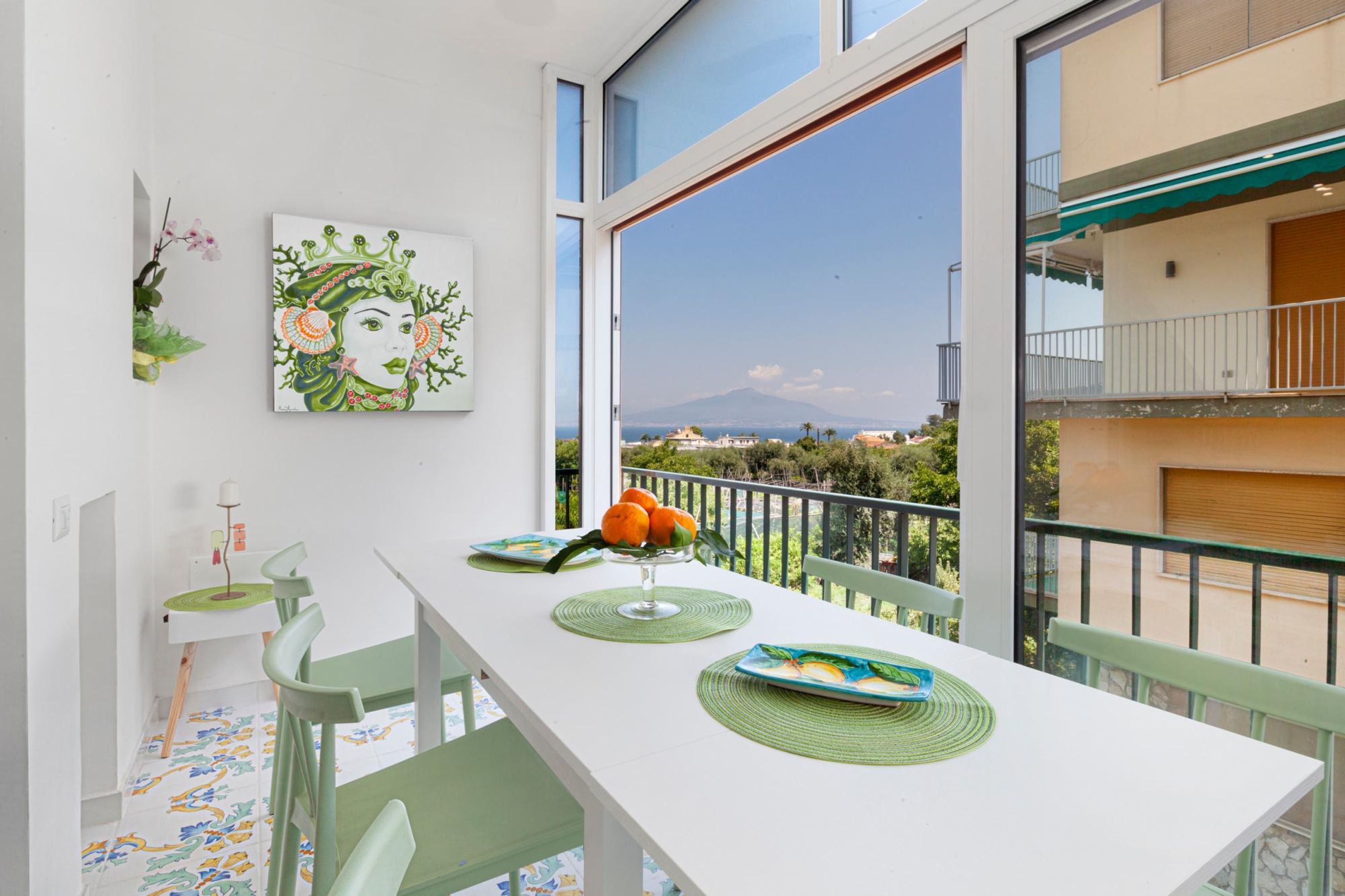 A dining area with a white table, green chairs, and a view of a mountain through large windows.