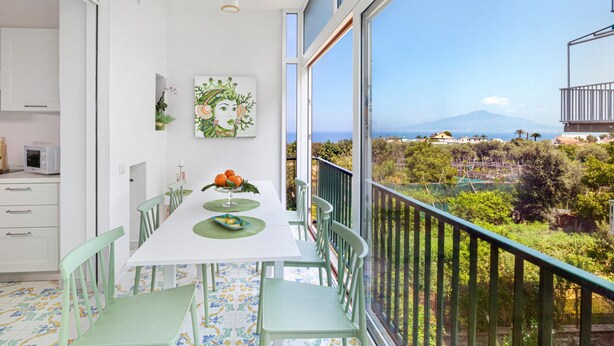 A dining area with a table and chairs, a view of a mountainous landscape, and a balcony with a railing. - Casa Maridea in Sorrento (Sorrento)