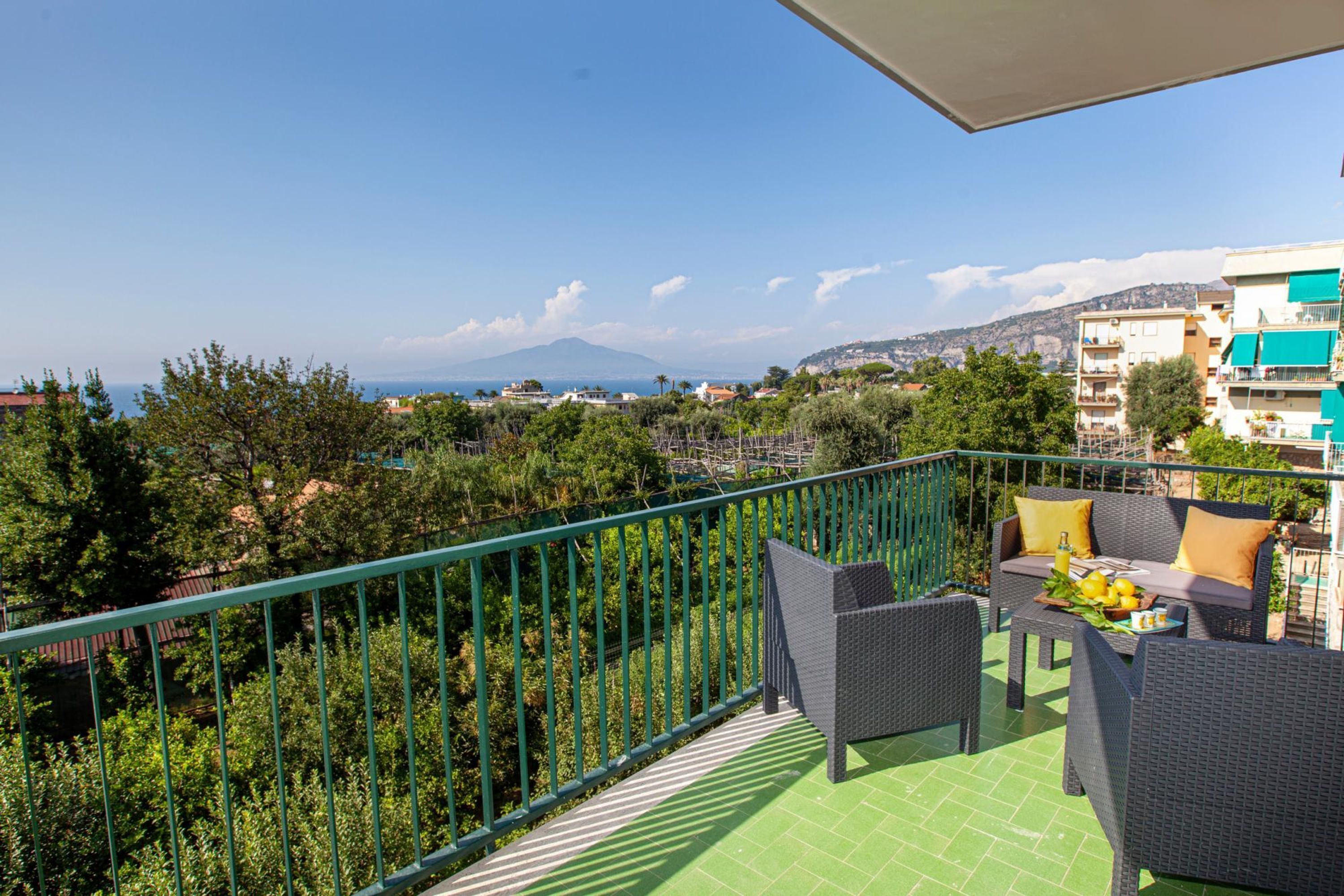 Ein Balkon mit Korbmöbeln, Blick auf das Meer und ein Berg in der Ferne.
