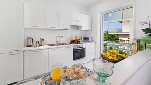 A modern kitchen with white cabinets, a microwave, and a dining area with a fruit bowl and glass pitcher. - Casa Maridea in Sorrento (Sorrento)