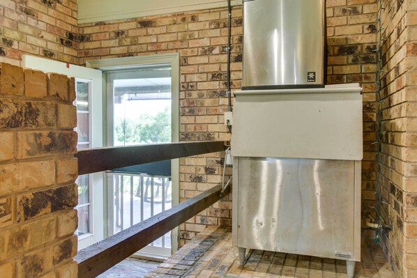 A kitchen with a stainless steel refrigerator, a brick wall, and a wooden railing.