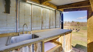 Een landelijke keuken met een metalen spoelbak, houten aanrechtblad en uitzicht op de omgeving.