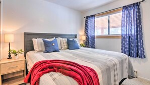 Ein Schlafzimmer mit Bett, Nachttisch, Lampe und einem Fenster mit Vorhängen.