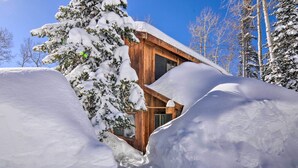 Eine Holzhütte, teilweise im Schnee versunken, mit blauem, wolkenlosem Himmel im Hintergrund.