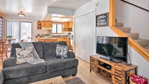 Ein modernes Wohnzimmer mit einem grauen Sofa, einem Flachbildfernseher und einer Treppe mit Holzwangen.