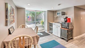 A compact kitchen with a microwave, toaster, and coffee maker on a shelf, a small refrigerator, and a dining area with a table and chairs. - Garden-level Millburn Apt - Walk to Transit! (Millburn)