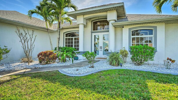 A modern house with a large front porch, a covered entryway, and a landscaped garden with palm trees and shrubs.