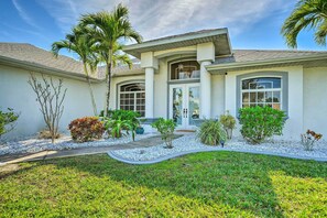 A modern house with a large front porch, a covered entryway, and a landscaped garden with palm trees and shrubs.