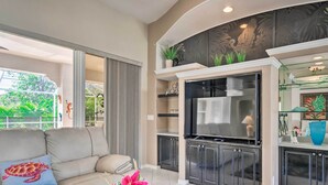 A modern living room with a sofa, a flat-screen TV, and a kitchen area with cabinets and a countertop.