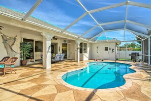 A covered outdoor swimming pool with a curved design, surrounded by a patio area with chairs and a potted plant.