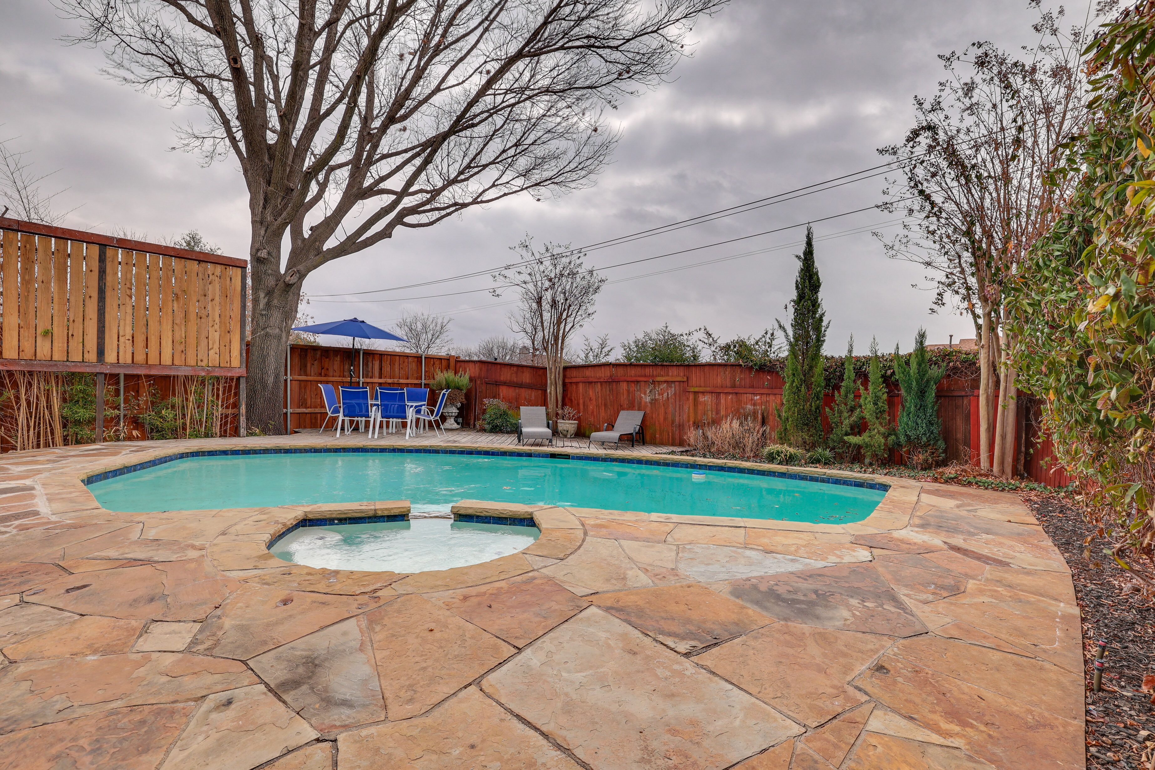 A backyard with a swimming pool, stone patio, and a wooden fence.