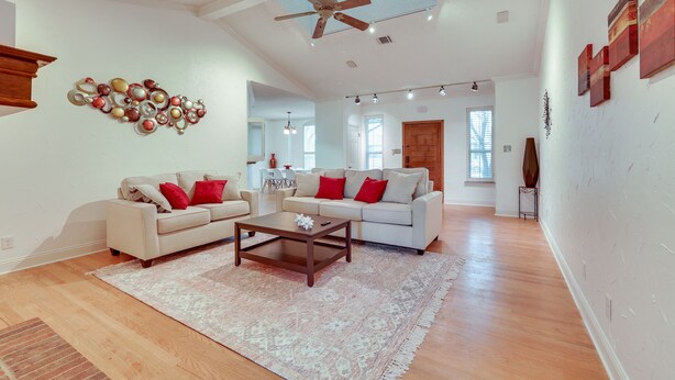 A spacious living room with a ceiling fan, two sofas with red cushions, a coffee table, and a patterned rug. - Modern Carrollton Home - Private Pool & Grill (Carrollton)