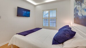 A bedroom with a bed, a window with blinds, a flat-screen TV on the wall, and a painting on the wall. - Modern Carrollton Home - Private Pool & Grill (Carrollton)