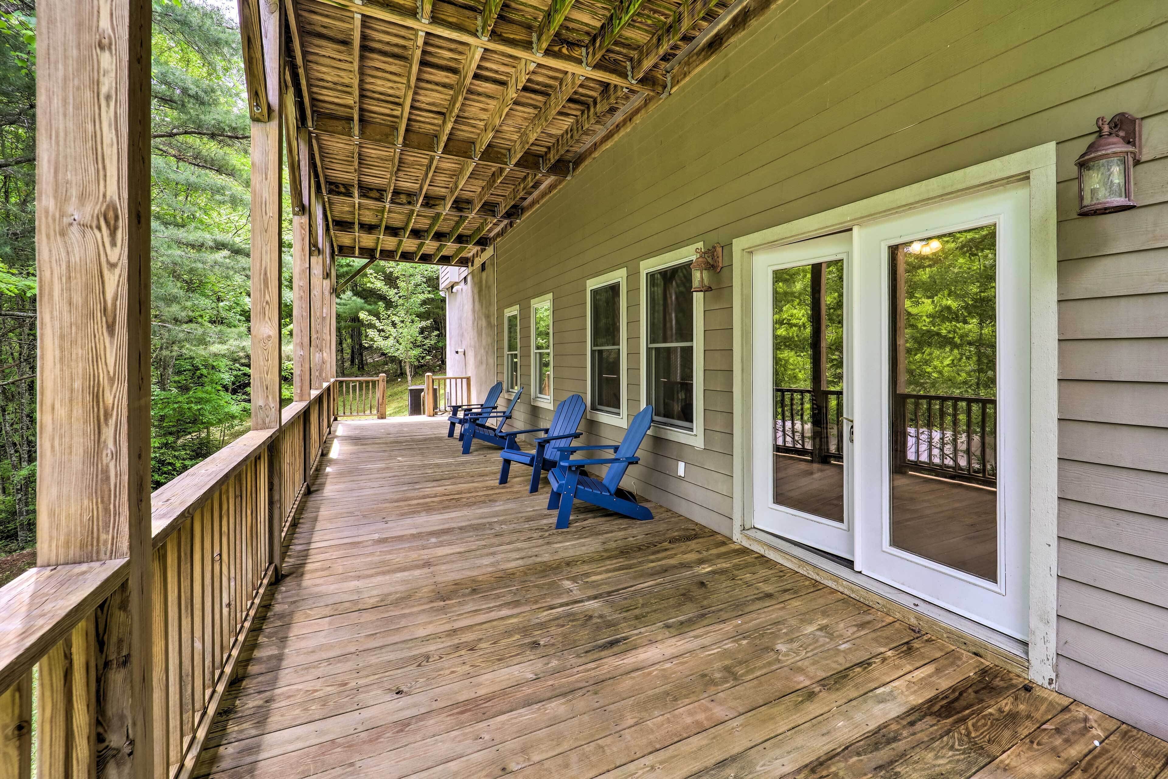 Une terrasse en bois avec des fauteuils Adirondack bleus, une véranda et une vue sur une zone boisée.