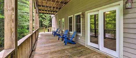 Une terrasse en bois avec des fauteuils Adirondack bleus, une véranda et une vue sur une zone boisée.