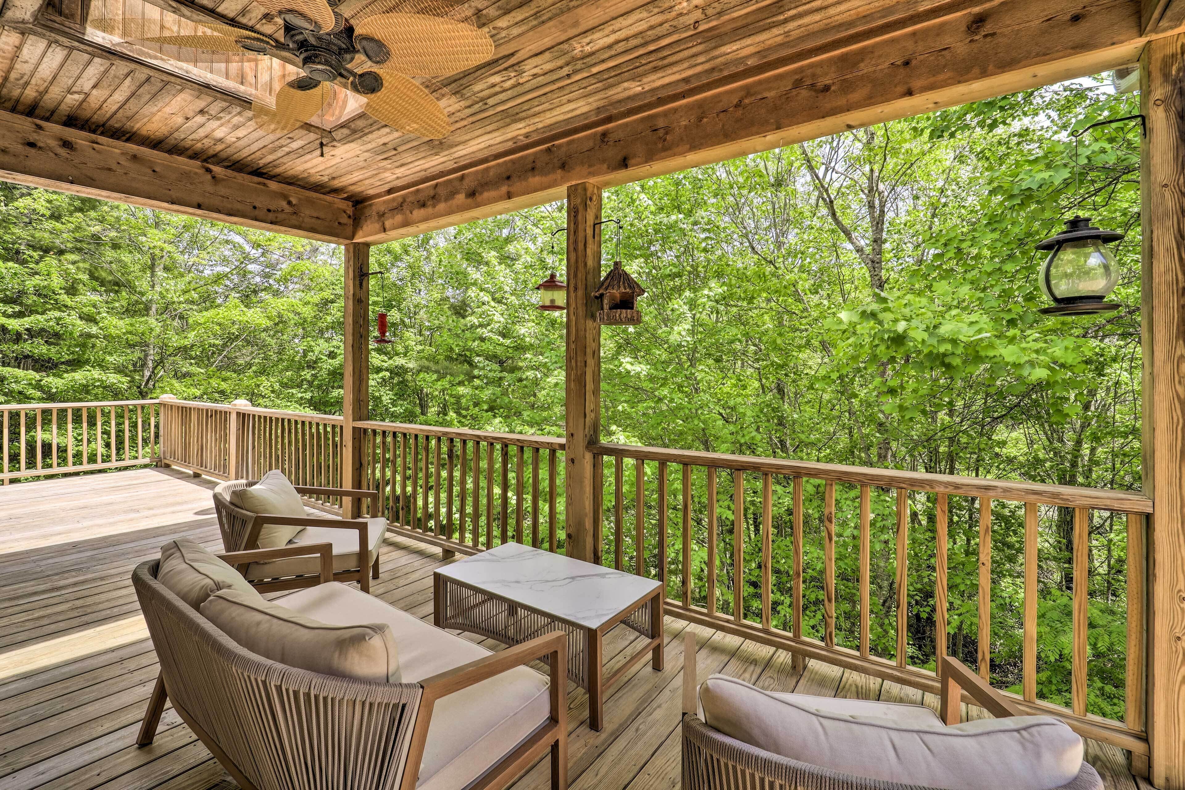 Eine Holzterrasse mit Korbmöbeln und einem Tisch, umgeben von einem Holgitter, mit Blick auf ein bewaldetes Gebiet.